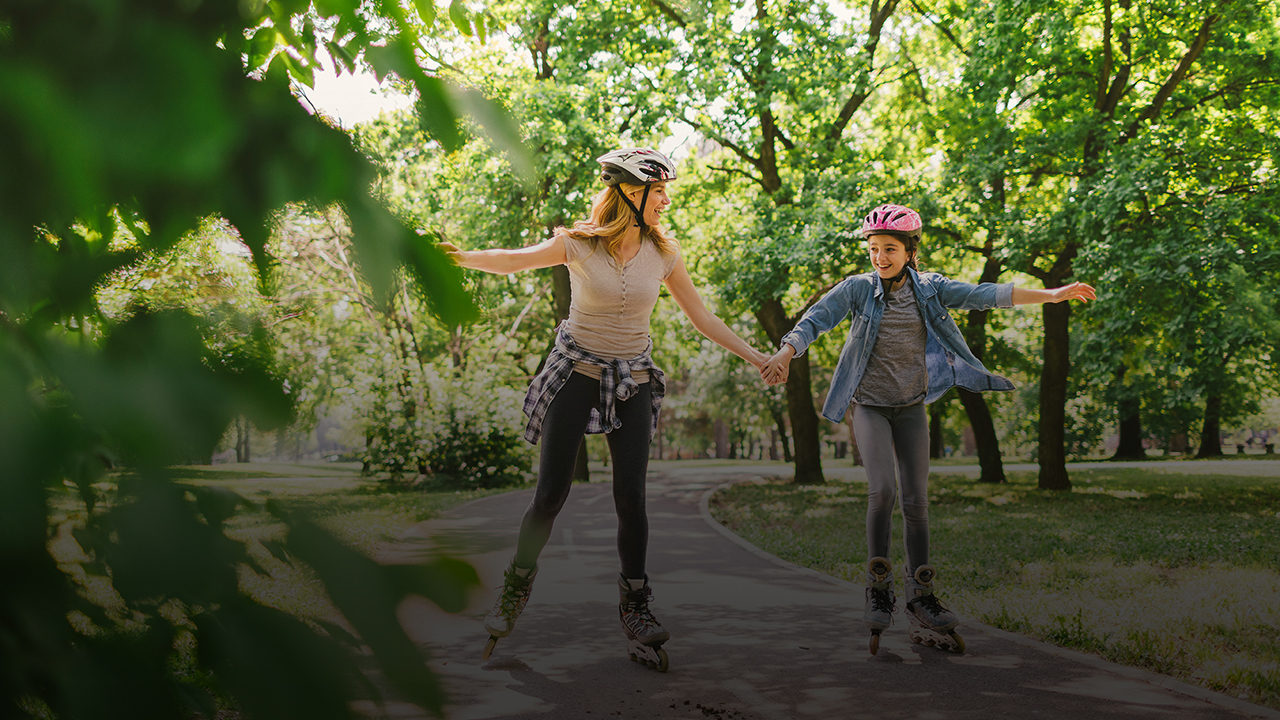 Eine Frau und ein Mädchen fahren mit Inline-Skates. Sie halten sich an der Hand.