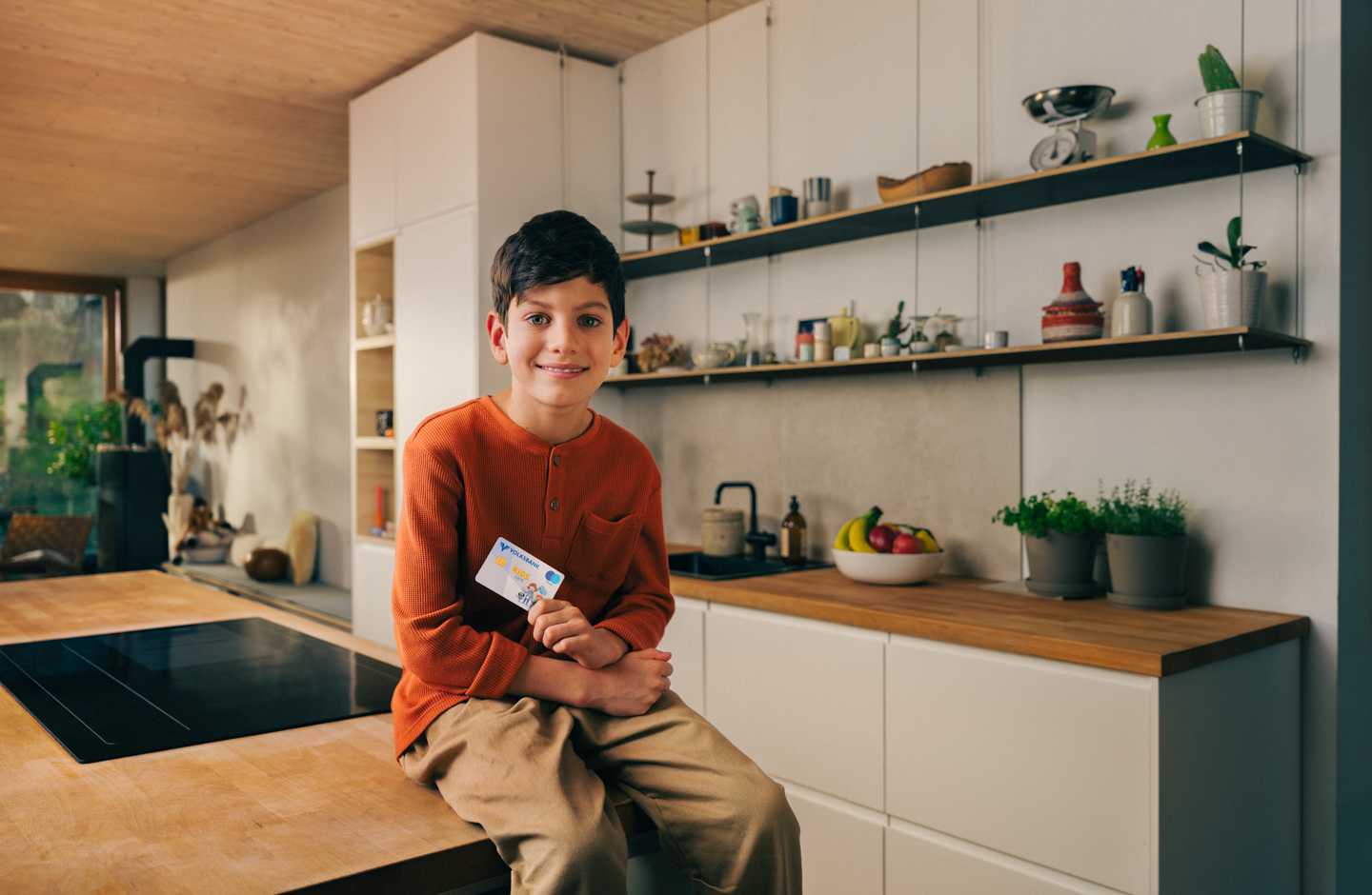 Ein Bub sitzt auf einem Tisch in der Küche und hält eine Volksbank Jugend Sparkarte in der Hand.