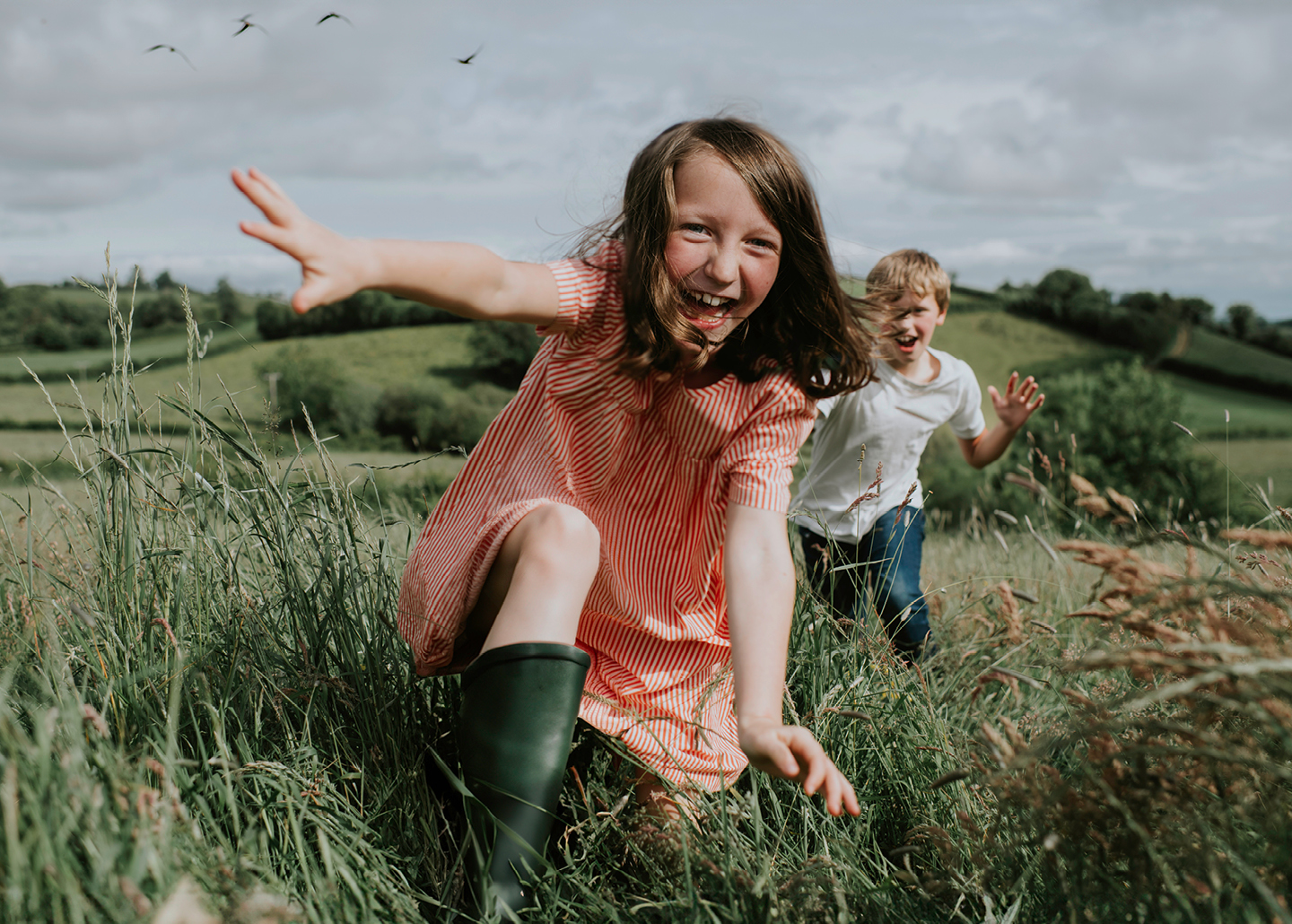 Ein Mädchen und ein Bub laufen über ein Feld auf die Kamera zu. Sie sind ausgelassen und lachen.
