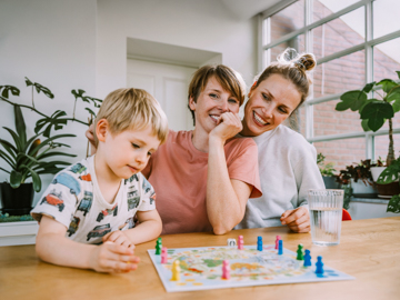 Zwei Frauen sitzen an einem Tisch und spielen Brettspiele mit einem Jungen.