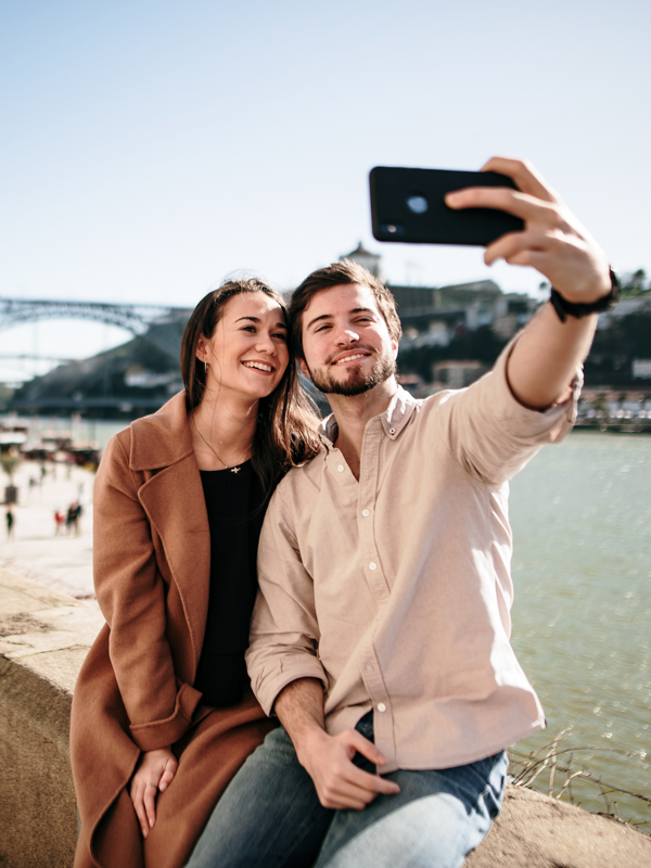 Eine Frau und ein Mann sitzen an einem Ufer und machen ein Selfie.
